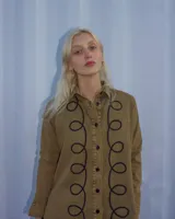 Camisa de denim celeste con bordado de líneas onduladas negras en el frente.