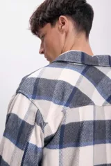 Sobrecamisa de franela a cuadros azul marino, gris y blanco, con cuello clásico, cierre frontal con botones, dos bolsillos de parche en el pecho y mangas largas con puños abotonados.
