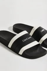 Sandalias de goma negras con banda ancha blanca con el logo de la marca.