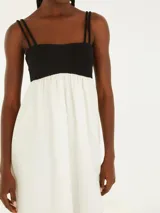 Vestido midi con tirantes finos, corte debajo del busto y falda amplia. La parte superior es negra y la falda es blanca.