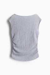 Top entallado color celeste en punto con textura. Modelo con escote bote, manga japonesa y costuras laterales fruncidas para un efecto drapeado suave.