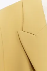 Blazer amarillo mostaza de cuello solapa y manga larga. Cierre frontal cruzado con botones forrados y bolsillos con solapa en delantero.