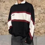 Chomba de manga larga negra con cuello polo blanco, franjas horizontales blancas y bordó, y detalles en blanco en los hombros.