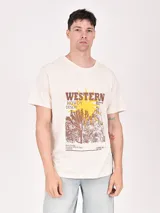 Remera color crudo con estampa frontal de estilo western con texto y paisaje desértico.