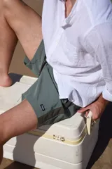 Short de baño verde con estampado de hojas y flores en tonos verde oscuro y marrón. Tiene bolsillos laterales y traseros, cintura elástica con cordón ajustable y corte clásico.