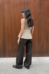 Top de punto acanalado en color beige, sin mangas y con cuello redondo. Presenta un cierre frontal con botones pequeños y un bajo con acabado en peplum que aporta volumen.