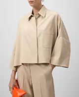 Camisa color beige de corte cuadrado y amplio, con cuello solapa, mangas 3/4 y bolsillo de parche en el pecho. Cierre frontal con botonadura oculta.