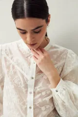 Camisa blanca con bordado floral en contraste, cuello mao, abotonadura frontal y mangas largas con frunces en los hombros.