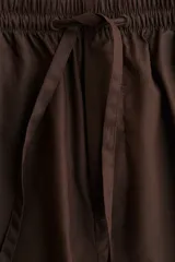 Pantalón marrón de algodón, corte holgado, tiro alto, cintura elástica fruncida con cordón ajustable, piernas anchas y bolsillos laterales.