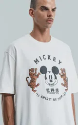 Remera blanca de algodón con cuello redondo y mangas cortas. Estampado frontal con diseño de Mickey Mouse, tigres y texto en inglés y chino.