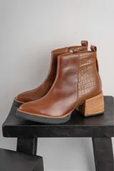 Bota corta de cuero marrón con puntera redondeada y taco cuadrado. Presenta una correa con hebilla alrededor del tobillo y cierre lateral.