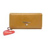 Billetera de cuero color camel con cierre de solapa y broche a presión. Logo de la marca en metal plateado y dije colgante en forma de corazón.