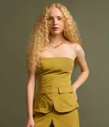 Blusa sin breteles color amarillo mostaza, confeccionada en sarga, con cierre por cremallera invisible en el lateral y bolsillos con solapa en la parte del frente. Posee lastex en la espalda y bajo redondeado.