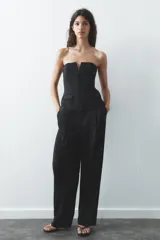 Top blanco de escote recto con detalle de pieza metálica en forma de V forrada y hombros descubiertos. Tiene falsos bolsillos con solapa en el delantero, forro interior combinado y cierre lateral con cremallera oculta en la costura.