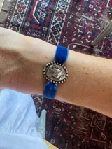 Pulsera con cinta de terciopelo azul y un dije ovalado de metal plateado con un relieve de la Virgen María.