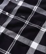 Camisa de franela para hombre con estampado de cuadros en blanco y negro. Tiene cuello inglés, mangas largas, bolsillos en el pecho y abotonado delantero.