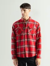 Camisa de franela con diseño a cuadros en tonos negro, rojo y blanco, con dos bolsillos frontales.
