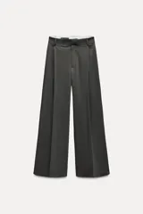 Pantalón de vestir gris oscuro, de tiro alto y corte palazzo. Presenta trabillas, bolsillos laterales y traseros de vivo, pliegues frontales y cierre frontal con cremallera, botón interior y ganchos metálicos.