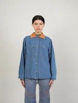 Campera de jean con cuello clásico, cierre frontal con botones metálicos, dos bolsillos de parche en el pecho y estampado floral en tonos verdes y marrones.