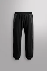 Pantalón de jogging negro con paneles laterales en gris oscuro, confeccionado en tejido técnico ligero y elástico. Cuenta con cintura elástica ajustable con cordón interior, bolsillos delanteros y bajo acabado en elástico ajustable con cremallera.