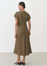 Vestido midi color verde oliva, de tejido fluido y diseño evasé. Presenta escote de pico, mangas cortas, cierre de cremallera invisible en la parte posterior y detalle drapeado en la cintura.