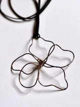 Collar con dije de alambre color bronce con forma de flor de cinco pétalos, colgando de un cordón negro.