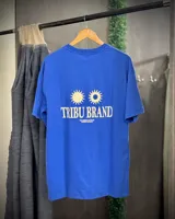 Remera azul con corte oversized, cuello redondo y estampado en el centro de la espalda con dos soles y la frase "TRIBU BRAND THE JOURNEY CONTINUES SUMMER VOLUME II".