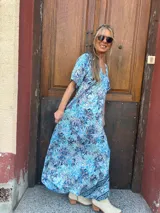 Vestido largo de seda con estampado floral en tonos turquesa, azul y blanco. Tiene escote en V y mangas cortas.