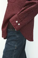 Camisa color borgoña a rayas verticales finas, de corte recto, con cuello solapa y manga larga. Tiene dos bolsillos de parche con solapa en el pecho y cierre frontal con botones.