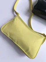 Cartera baguette de cuero sintético color amarillo pastel, con correa de hombro del mismo material y cierre superior.
