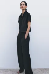 Pantalón negro de tiro medio con trabillas en la cintura, bolsillos delanteros, pierna recta y cierre frontal con cremallera, botón y gancho metálico.