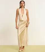 Vestido largo de satén color crema, con escote halter, espalda descubierta y abertura frontal. Presenta detalles de pedrería en el escote.