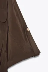 Camisa marrón de cuello solapa y manga corta con trabilla y botón. Tiene bolsillos delanteros de plastrón con solapa, bajo elástico y cierre frontal con botones a presión.
