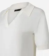Blusa de punto color blanco, con cuello polo, escote en V y mangas cortas. Detalle de mini perlas aplicadas en el cuello.