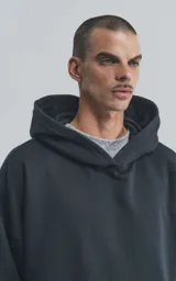 Hoodie negro de corte oversize con capucha, bolsillo tipo canguro y detalle de bolsillo con cierre en la manga izquierda.