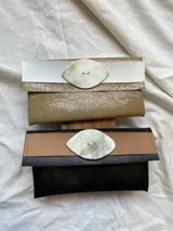 Billetera tipo sobre de ecocuero color beige con textura craquelada y solapa con aplique de cuero liso y botón de guampa.