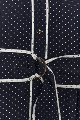Vestido midi azul marino con estampado de lunares blancos, cuello solapa, escote en pico y sin mangas. Incluye cinturón de la misma tela y cierre frontal con botones.