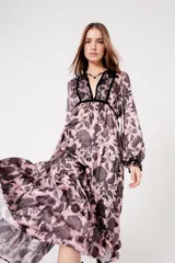 Vestido largo rosado con estampado floral negro, escote en V con ribete negro, mangas largas abullonadas y falda escalonada con volantes.