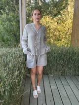 Camisa blanca de lino con cuello mao, mangas largas abullonadas y cierre frontal con botones de nácar. Presenta volados en el frente y puños elásticos.