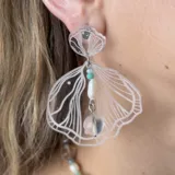 Par de aros colgantes con forma de concha marina transparente con detalles lineales blancos, cuentas de colores y dije de esfera transparente.