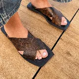 Sandalias bajas color marrón con base negra y tiras anchas cruzadas de cuero sintético con textura.