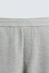 Pantalón de jogging gris con corte relaxed fit, cintura elástica ajustable con cordón interior, bolsillos laterales y traseros de vivo, y banda lateral color crema.