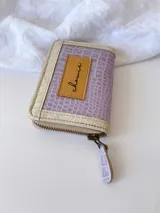 Billetera pequeña con cierre metálico, cuerpo principal de cuero lila texturizado y ribetes en color crema. Presenta un parche de cuero marrón con la palabra "chowie" escrita en cursiva.