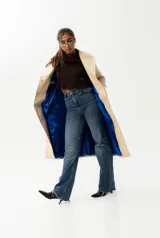 Trench largo de cuero color beige con forro azul, cuello clásico, cierre frontal con botones y bordado de las "S" en el frente.