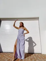 Vestido largo lila con escote halter cruzado en la espalda y falda tipo pareo con abertura lateral y nudo decorativo.