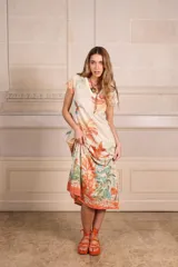 Vestido largo color crudo con estampado tropical en tonos naranja, verde y celeste. Tiene escote en V, mangas cortas y corte recto. Incluye lurex dorado.