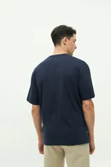 Remera color marrón con cuello redondo y manga corta. Presenta un bordado en el lado izquierdo del pecho con un diseño abstracto y texto.