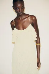 Vestido midi color crema confeccionado en encaje, con escote recto, tirantes finos, volantes y tachas.