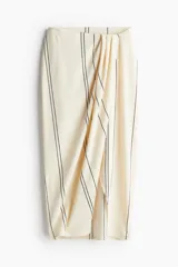 Pollera midi color crema con rayas verticales negras, de punto con textura. Diseño cruzado con elástico oculto en la parte posterior de la pretina y sección delantera cosida con pliegues para crear un leve efecto drapeado.