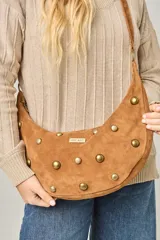 Cartera tipo bandolera de cuero sintético color celeste, con forma de media luna y tachas metálicas redondas plateadas en el frente. Posee correa ajustable y placa metálica con logo en la parte superior.